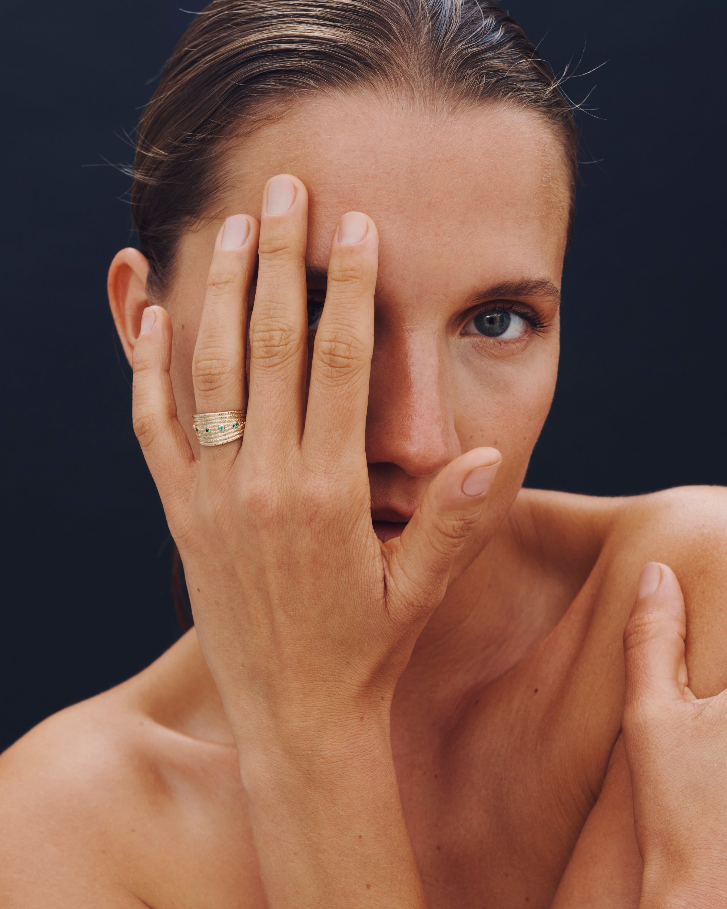 Woman with a gold ring on her finger against a dark background