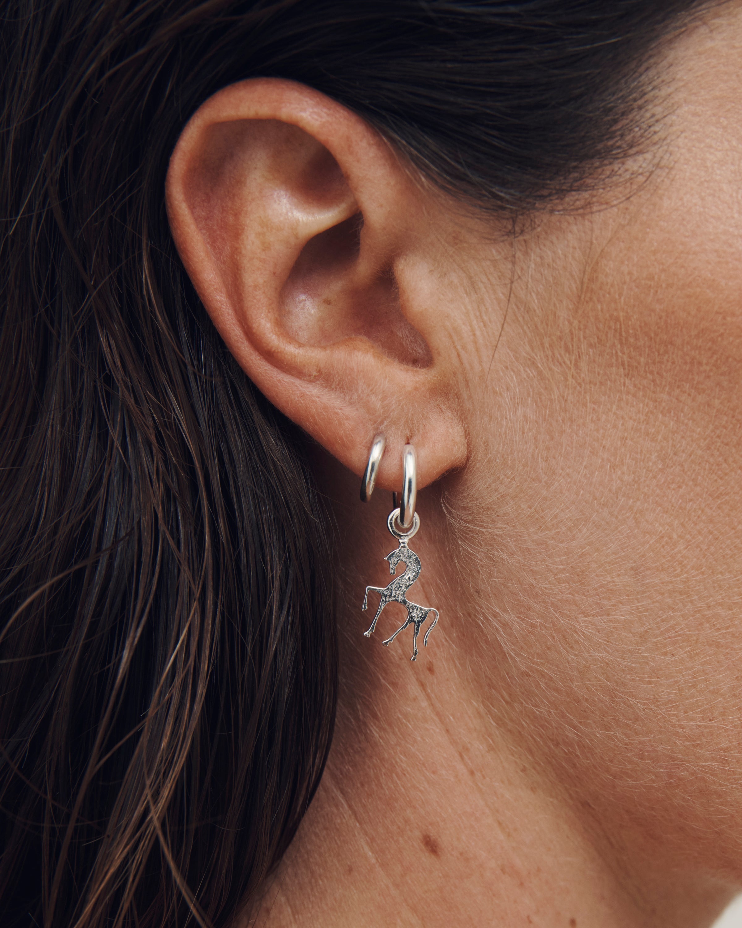 Close-up of an ear wearing a silver hoop earring with a small pendant.