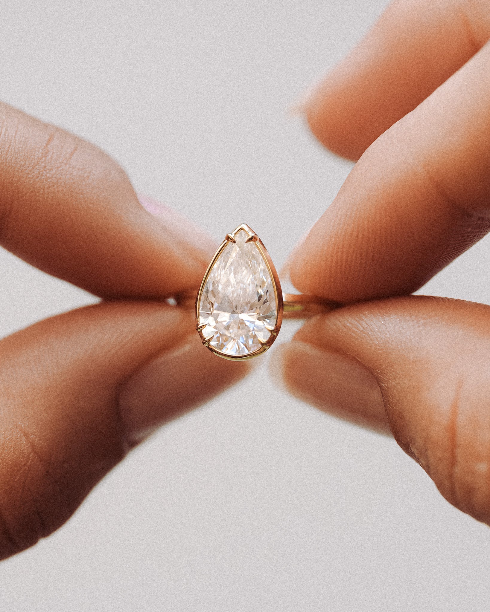 Teardrop-shaped diamond ring held between fingers on a light background