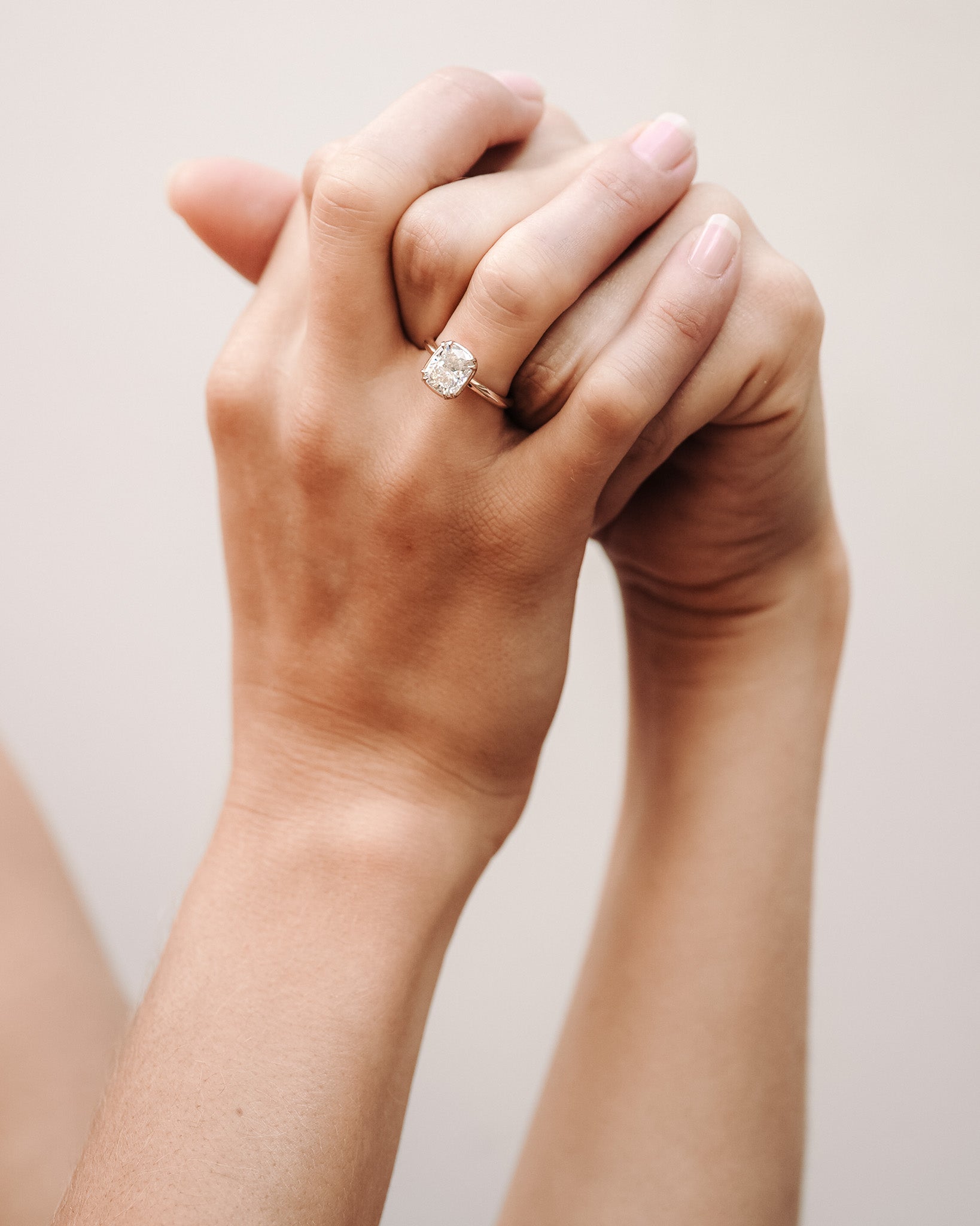 Close-up of two hands interlocked with a diamond ring on a neutral background