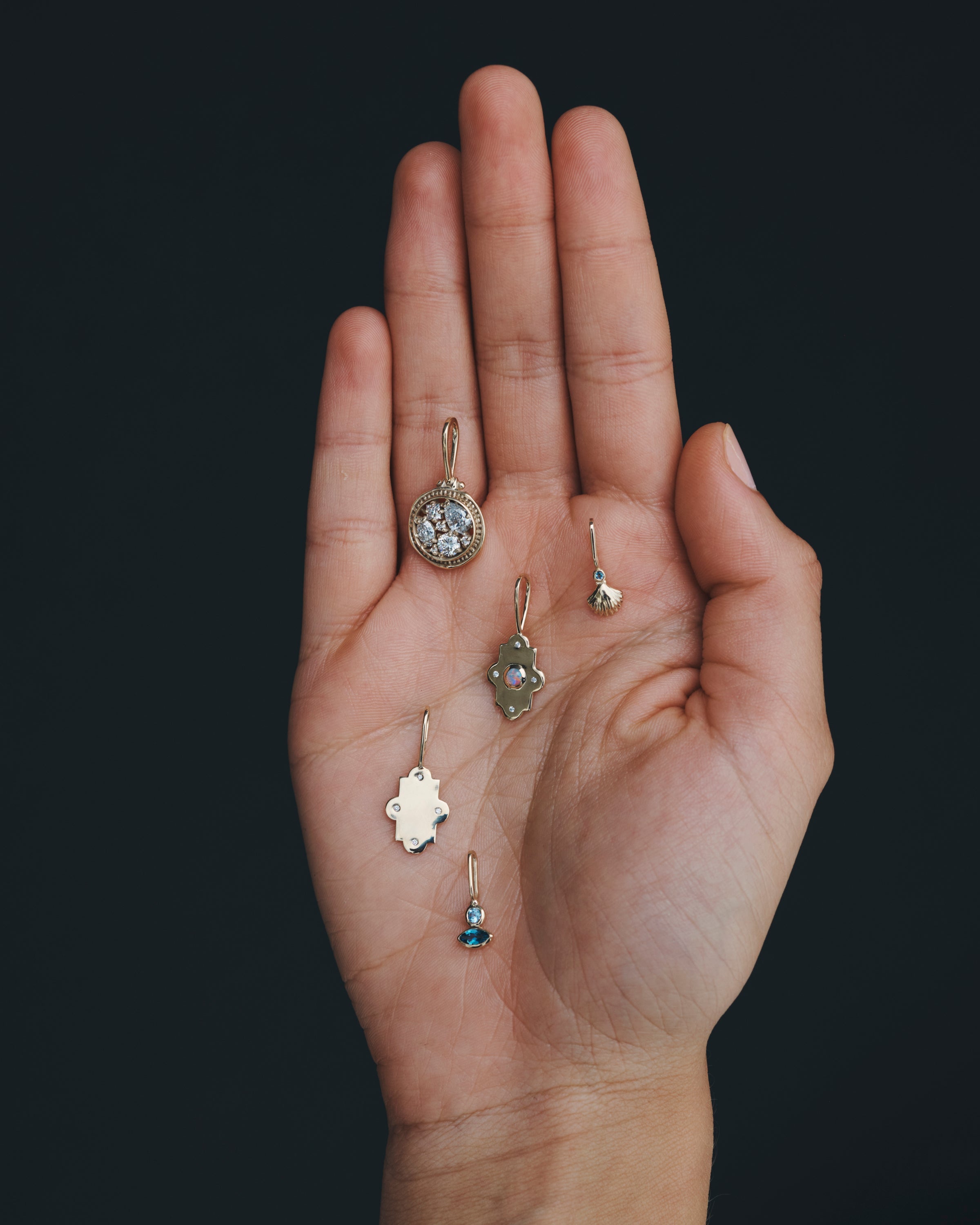 Hand holding various small earrings against a dark background