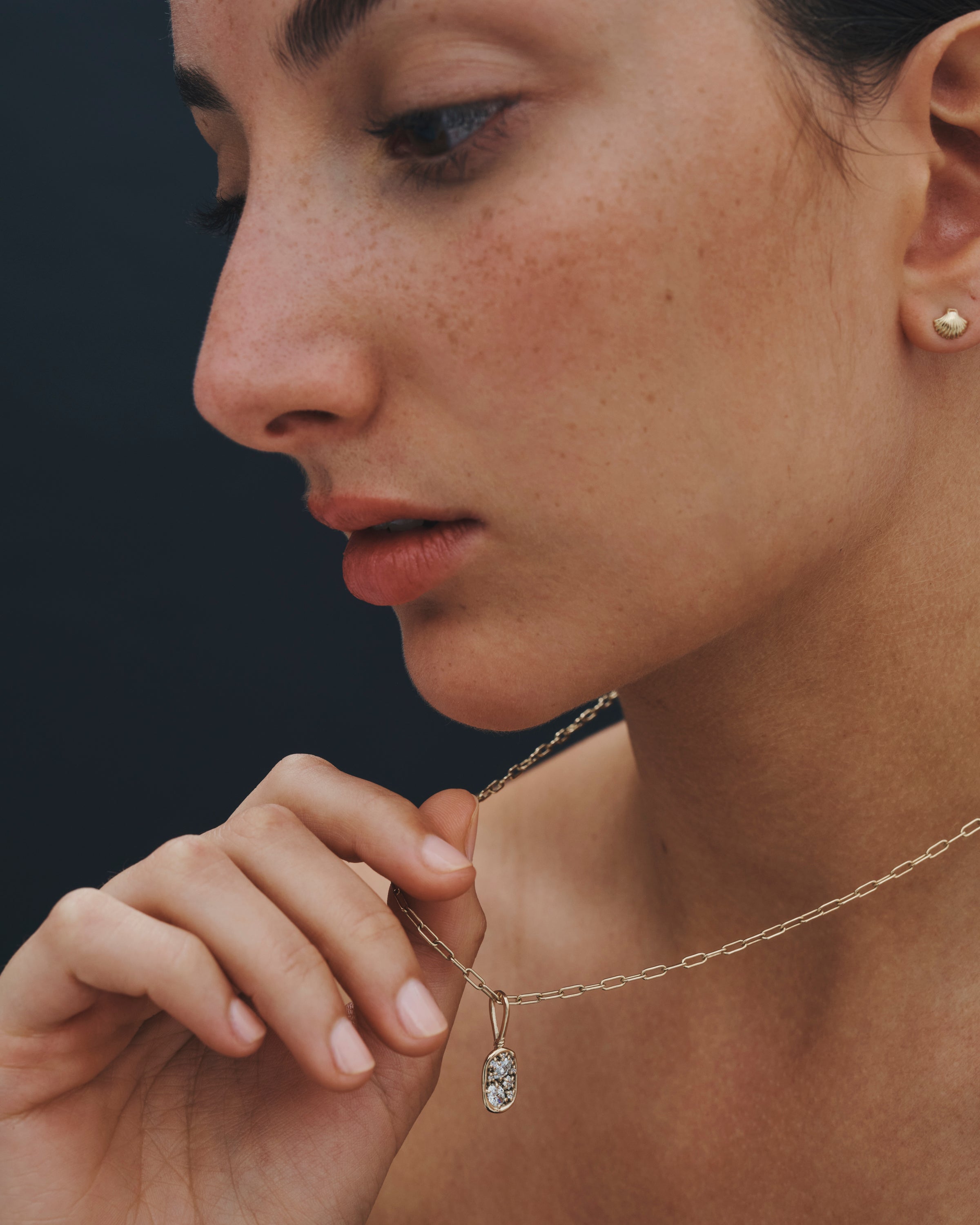 Close-up of a woman wearing a gold necklace with a pendant against a dark background