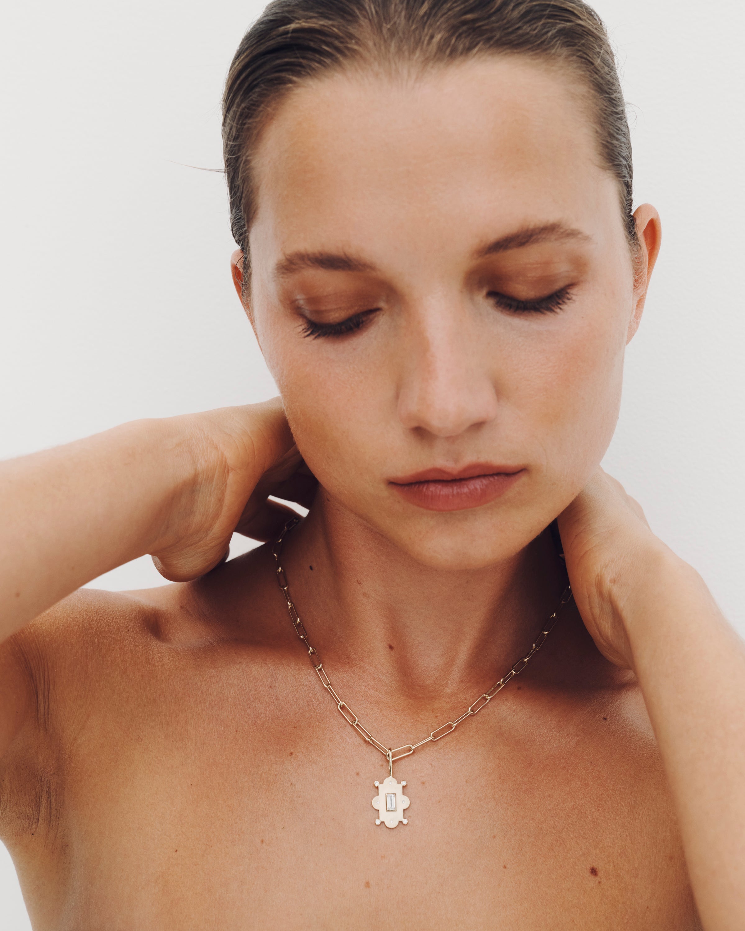 Woman wearing a necklace with a white pendant on a plain background