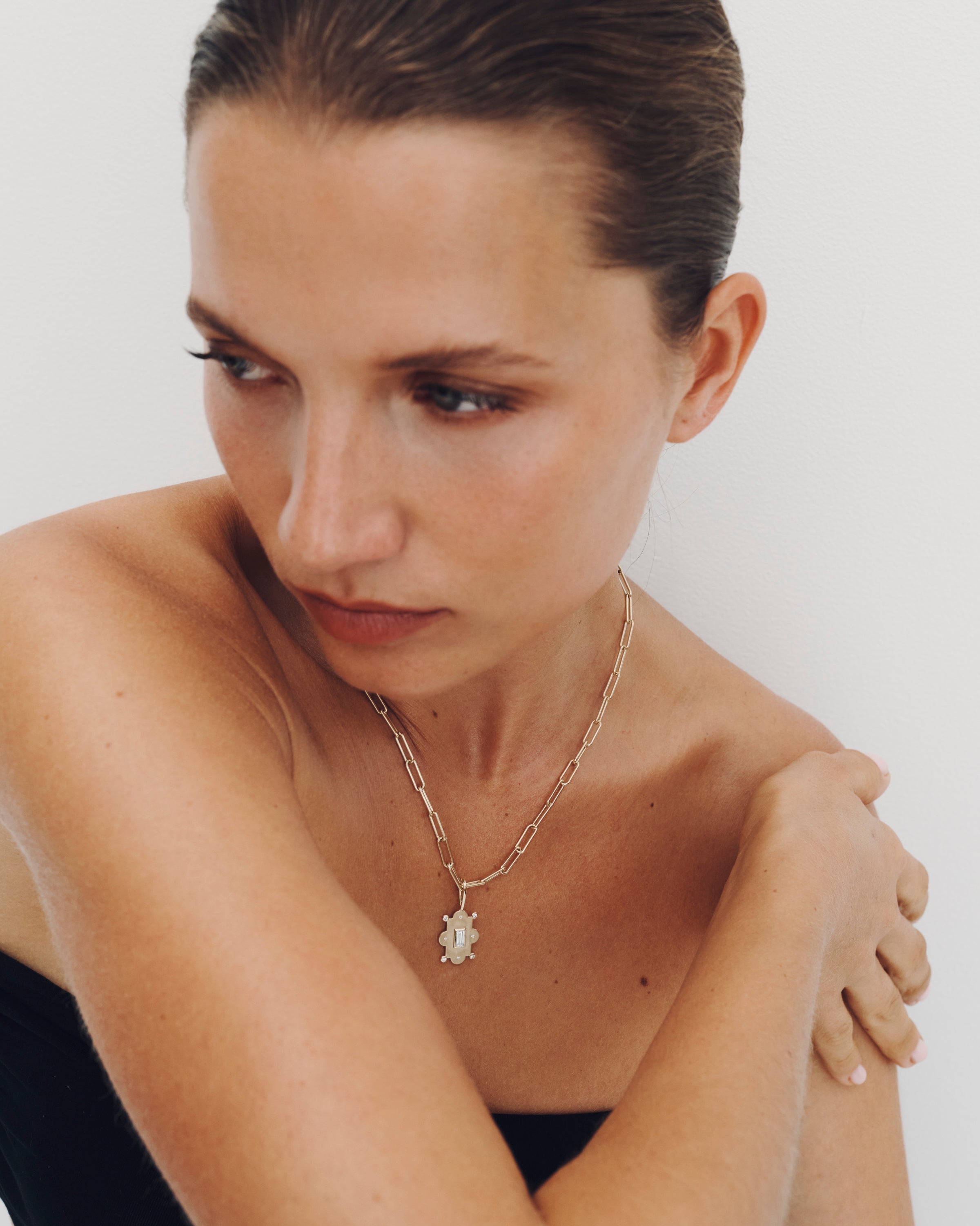 Woman wearing a necklace with a pendant against a plain background