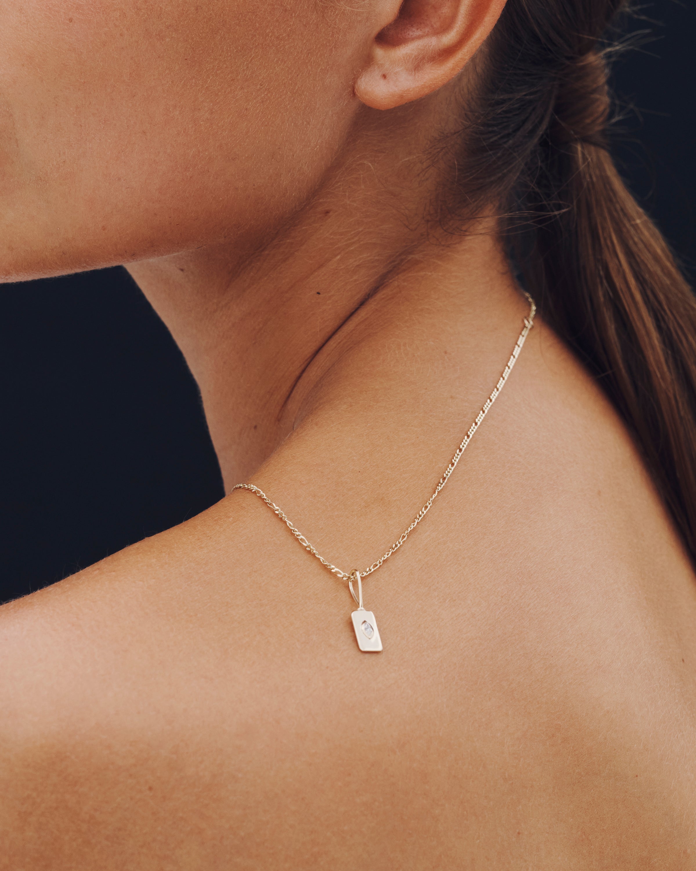 Gold necklace with a small pendant on a person's neck against a dark background