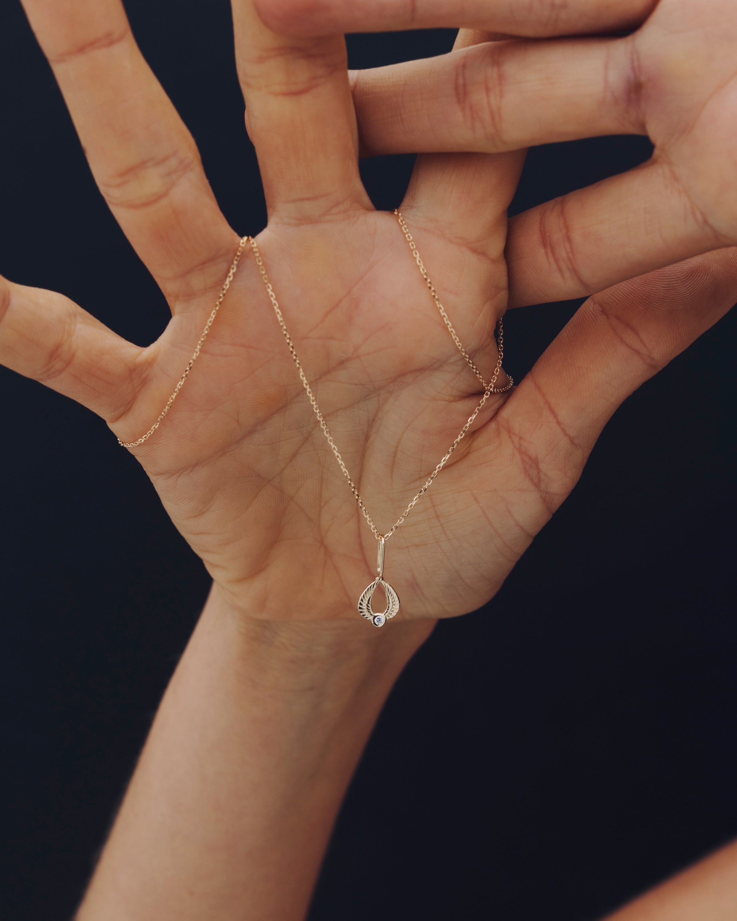 Gold necklace with a pendant held in a hand against a dark background