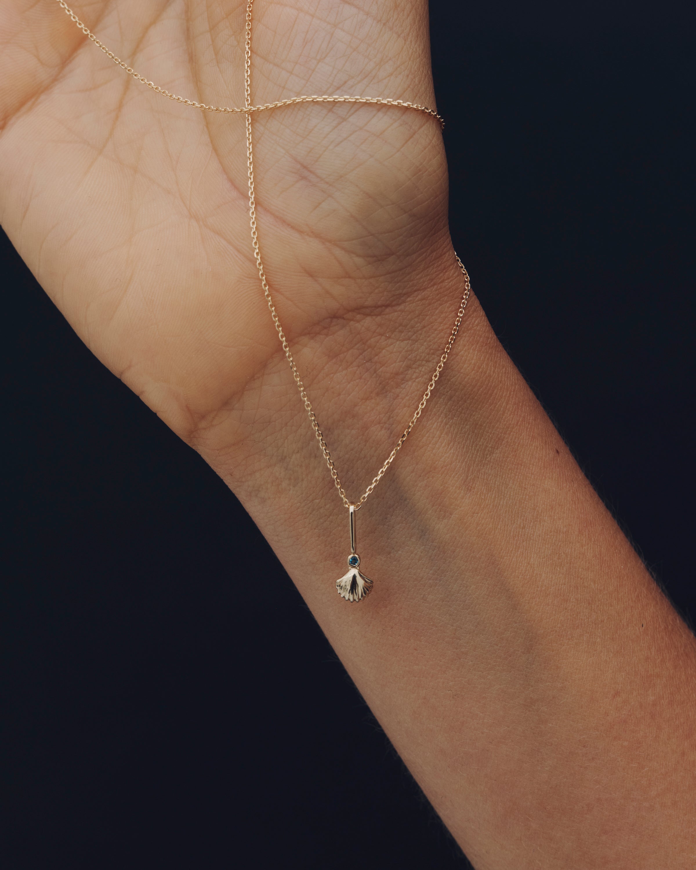 Gold necklace with a small pendant on a wrist against a dark background