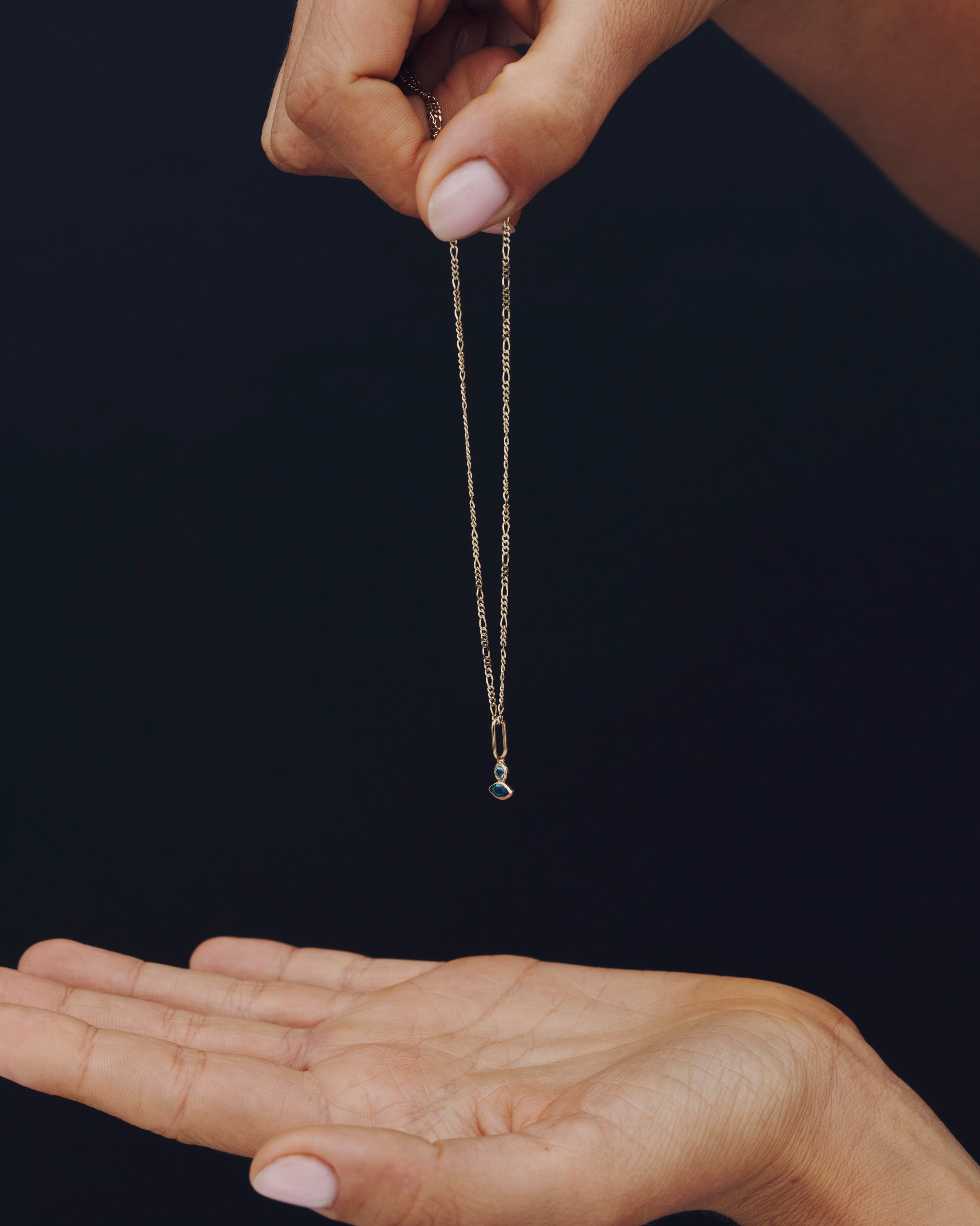 Hand holding a necklace with a clear pendant against a black background