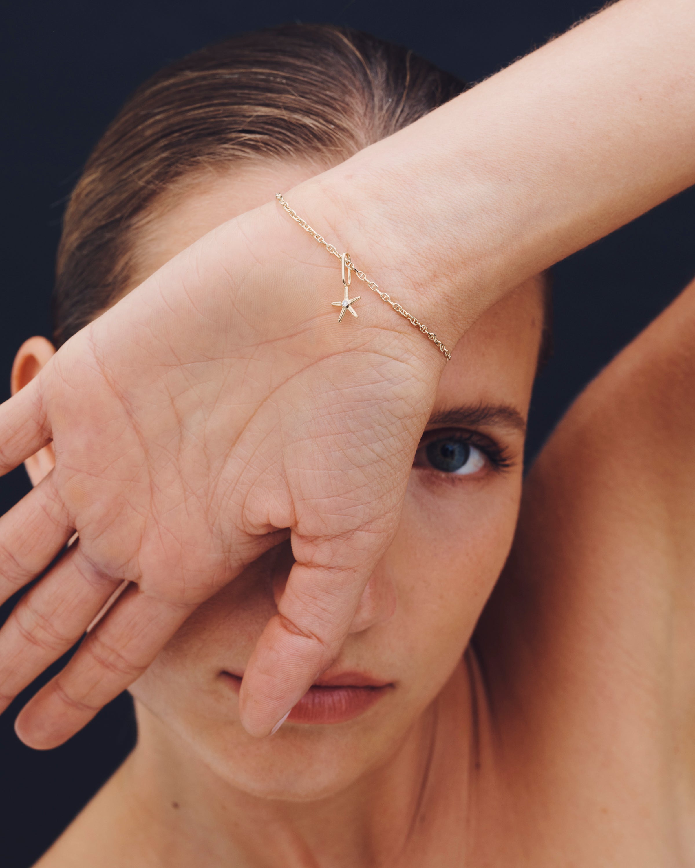 Woman wearing a gold bracelet with starfish charm on a dark background