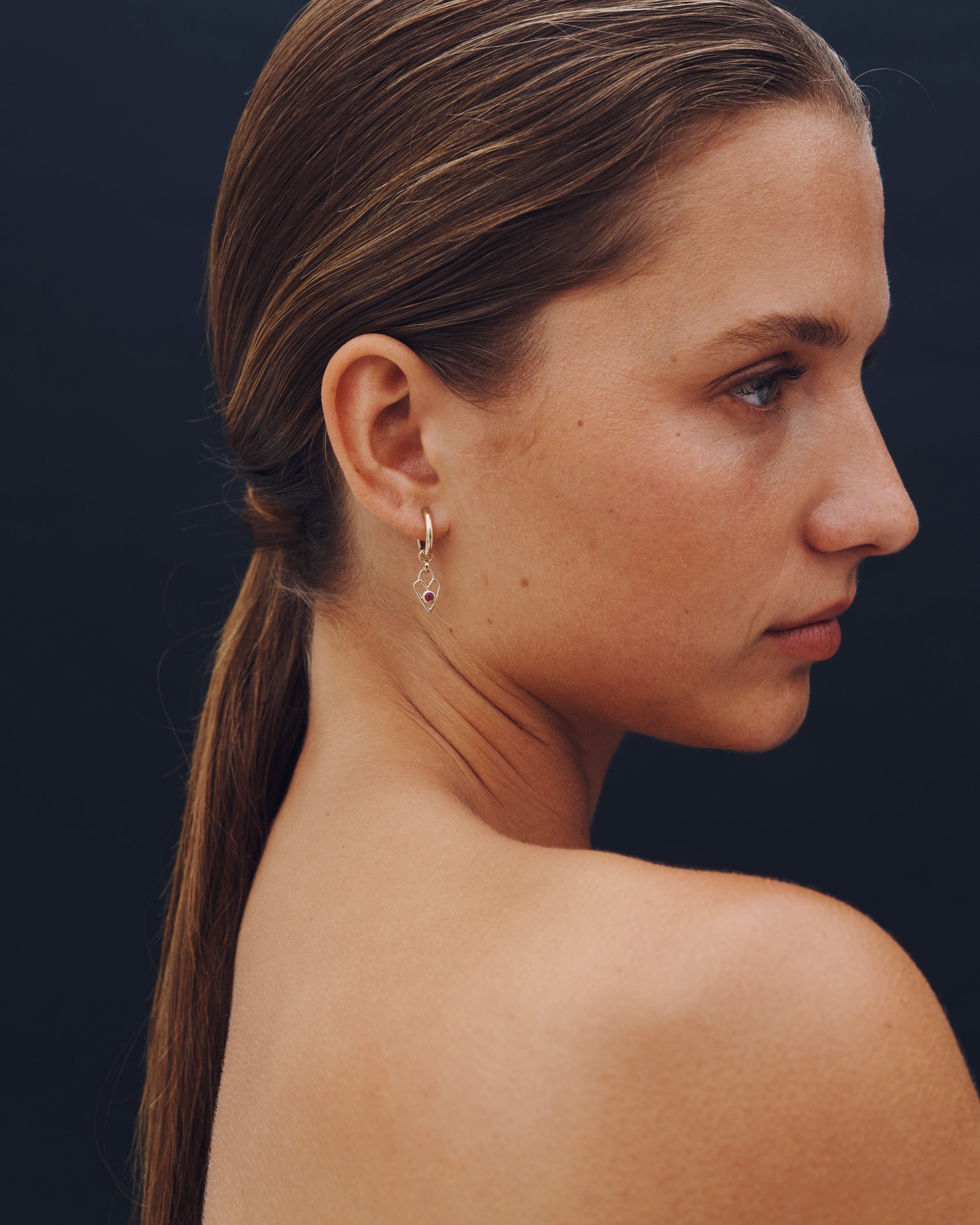 Woman with a ponytail wearing an earring against a dark background