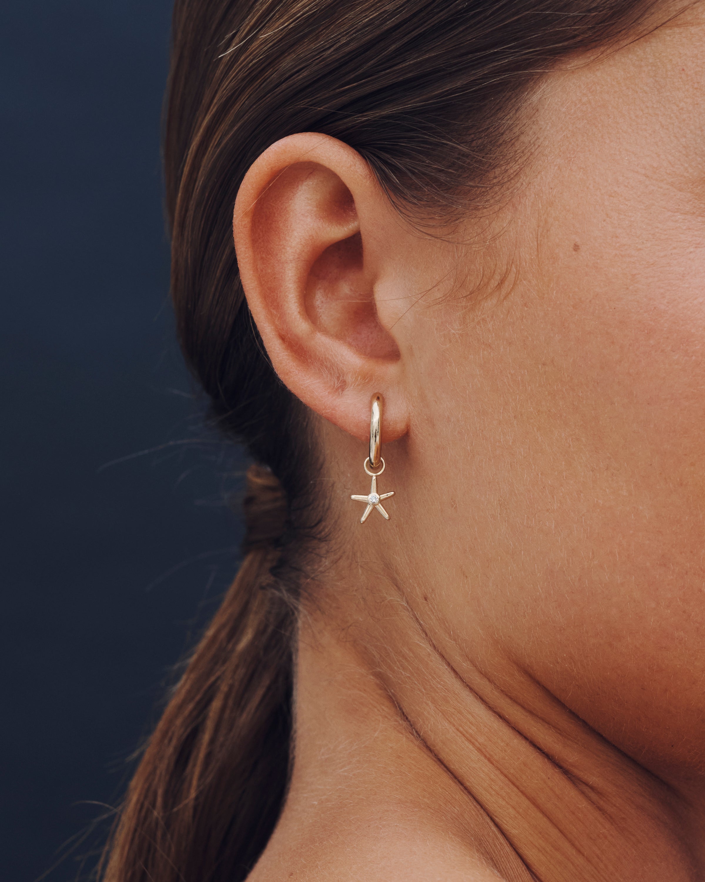 Close-up of an ear wearing a starfish-shaped earring against a dark background