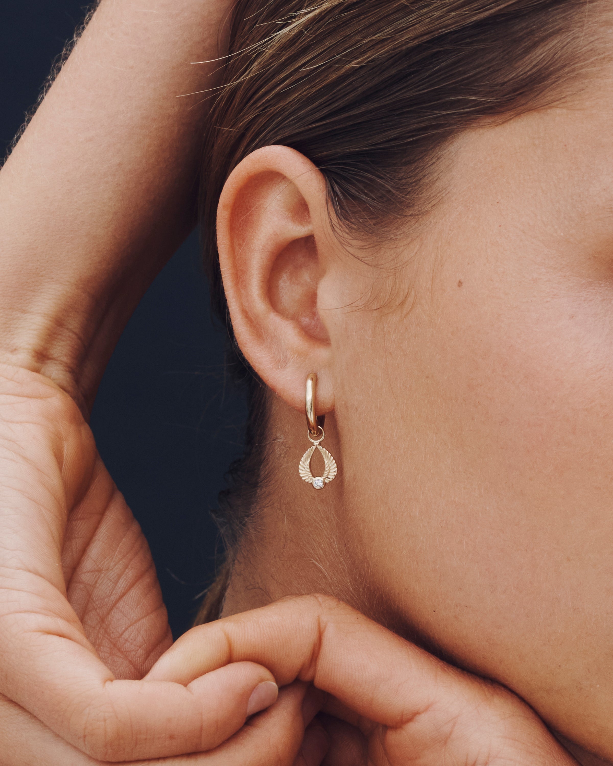 Close-up of a person wearing a gold hoop earring with a dark background