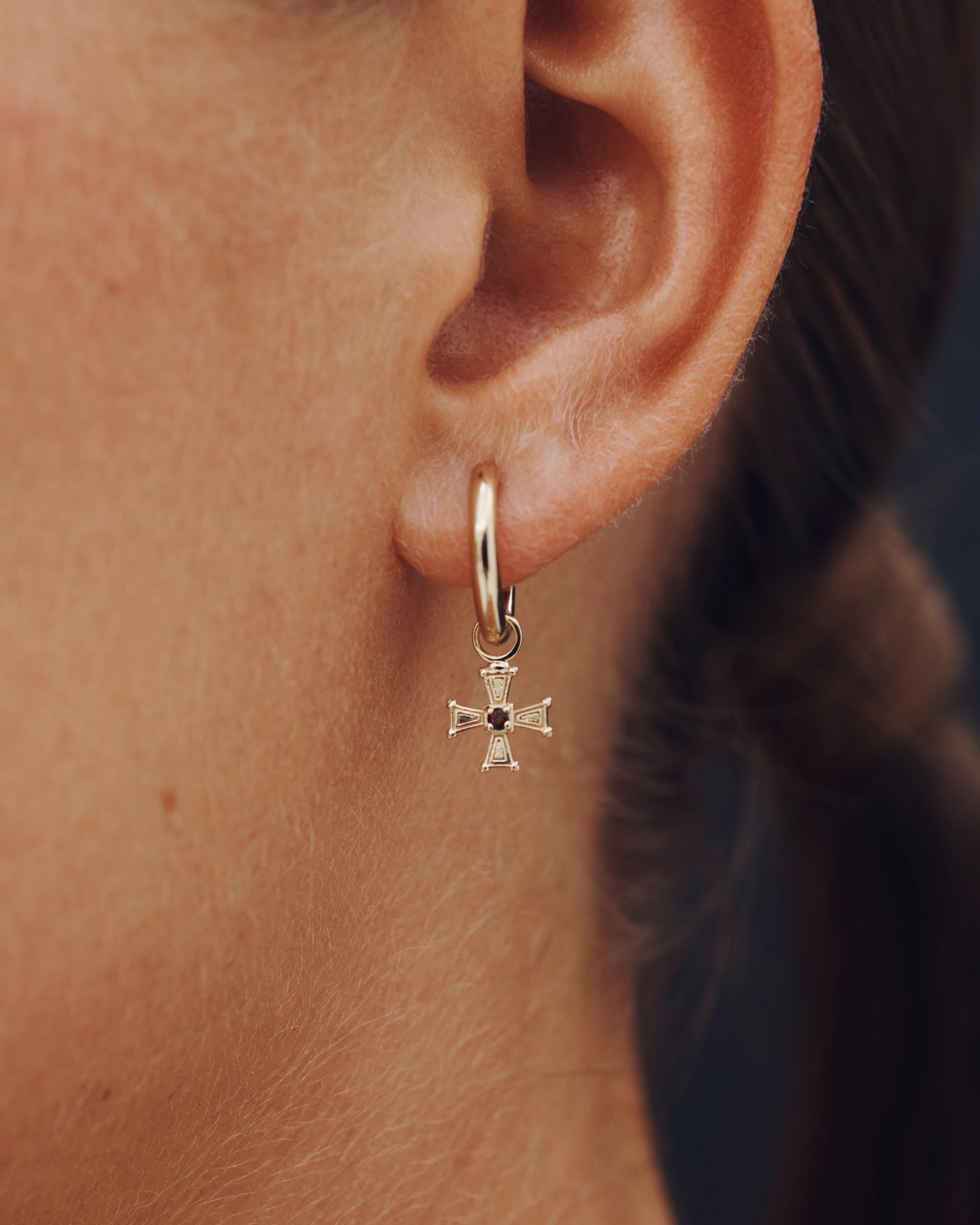 Gold hoop earring with a cross pendant worn by an ear