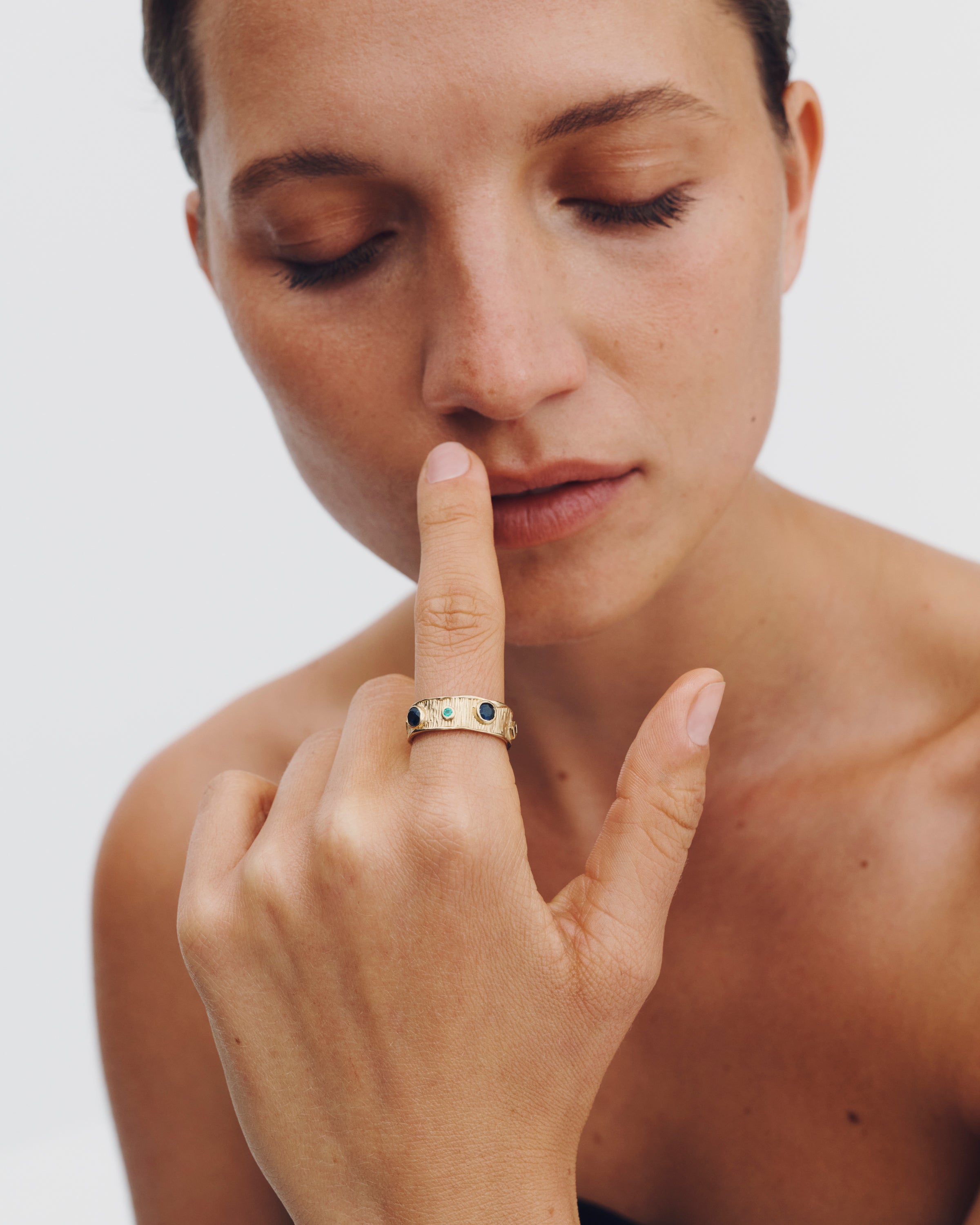 Woman wearing a gold ring with gemstones on her finger against a plain background