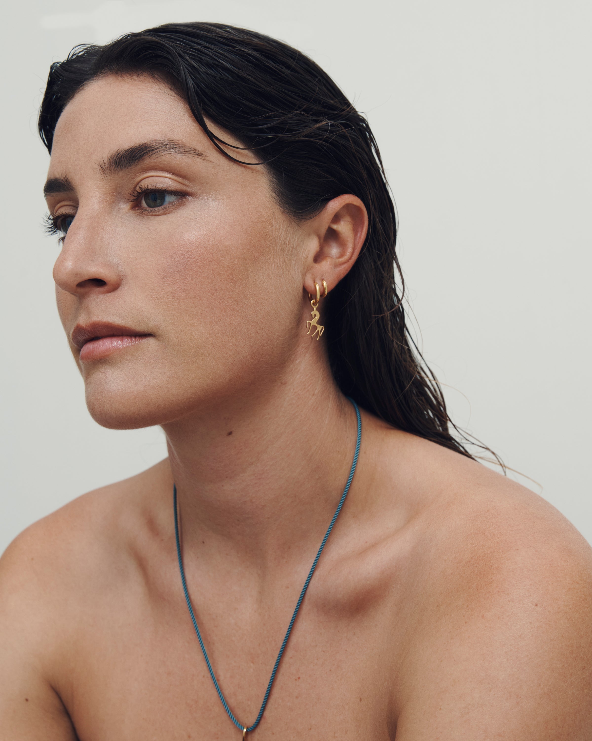 Woman wearing a necklace and gold hoop earrings against a plain background