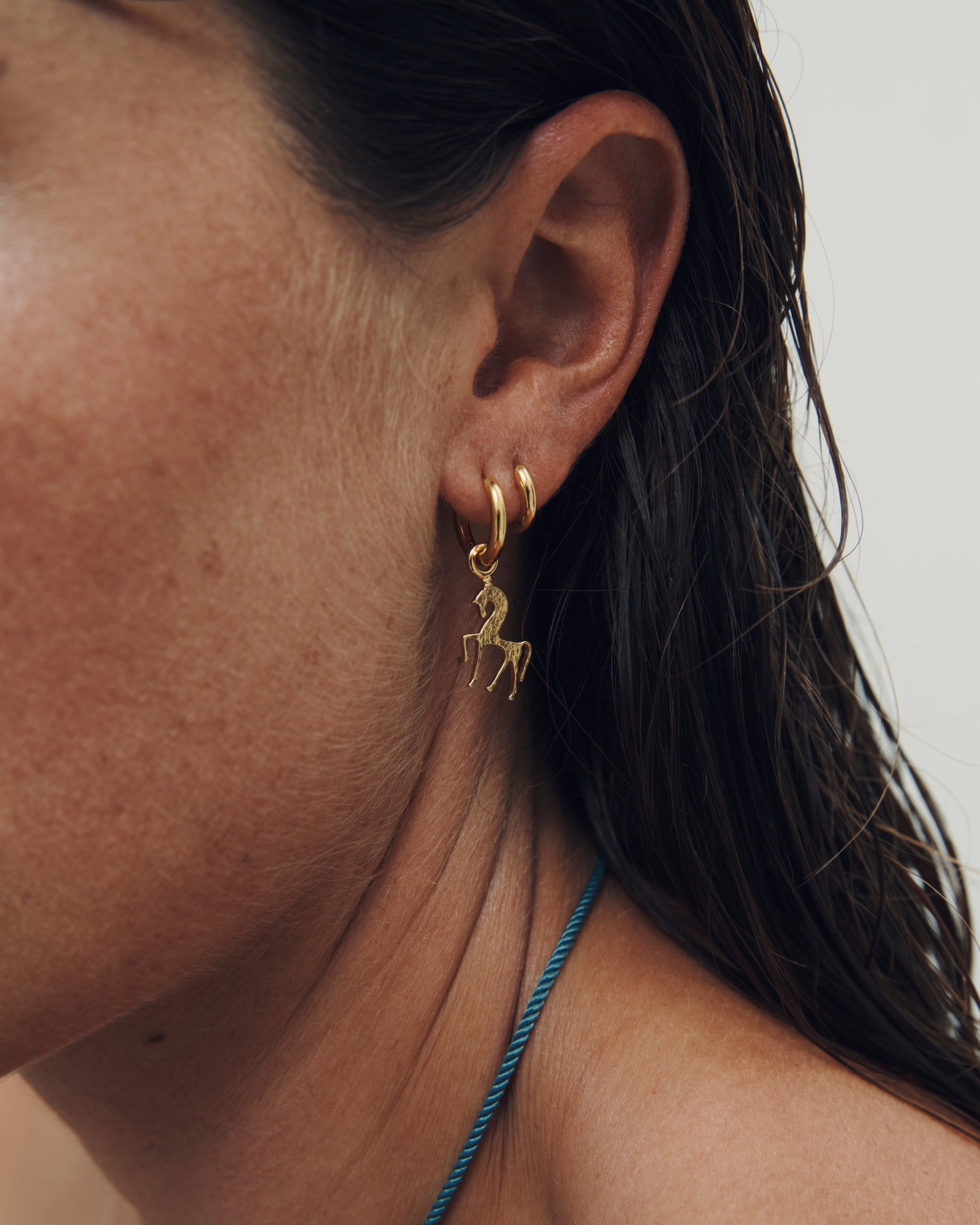 Close-up of a person wearing a gold hoop earring with a small charm.