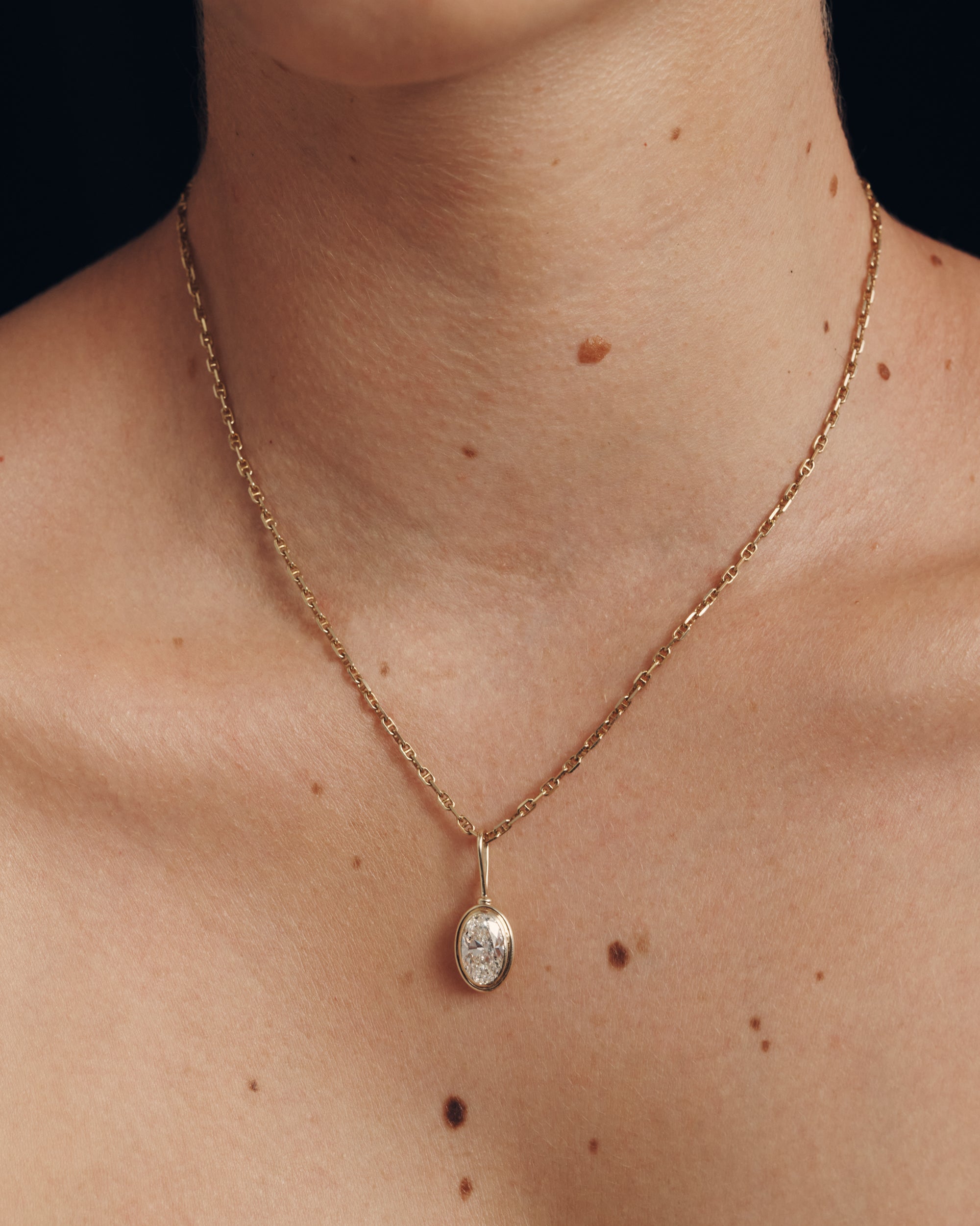 Gold necklace with a pendant on a person's neck against a black background