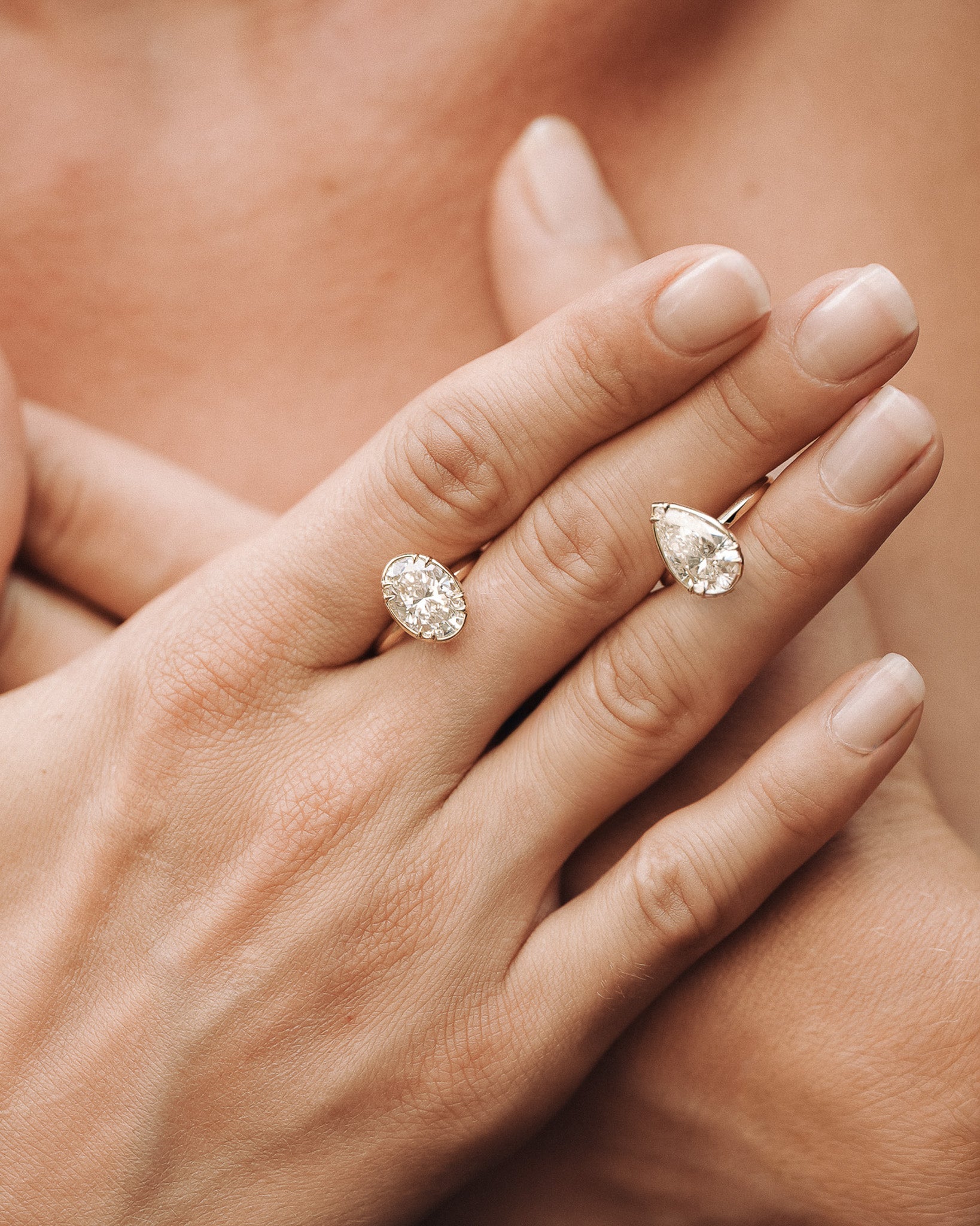 Close-up of a hand wearing two pear-shaped diamond rings on a blurred background