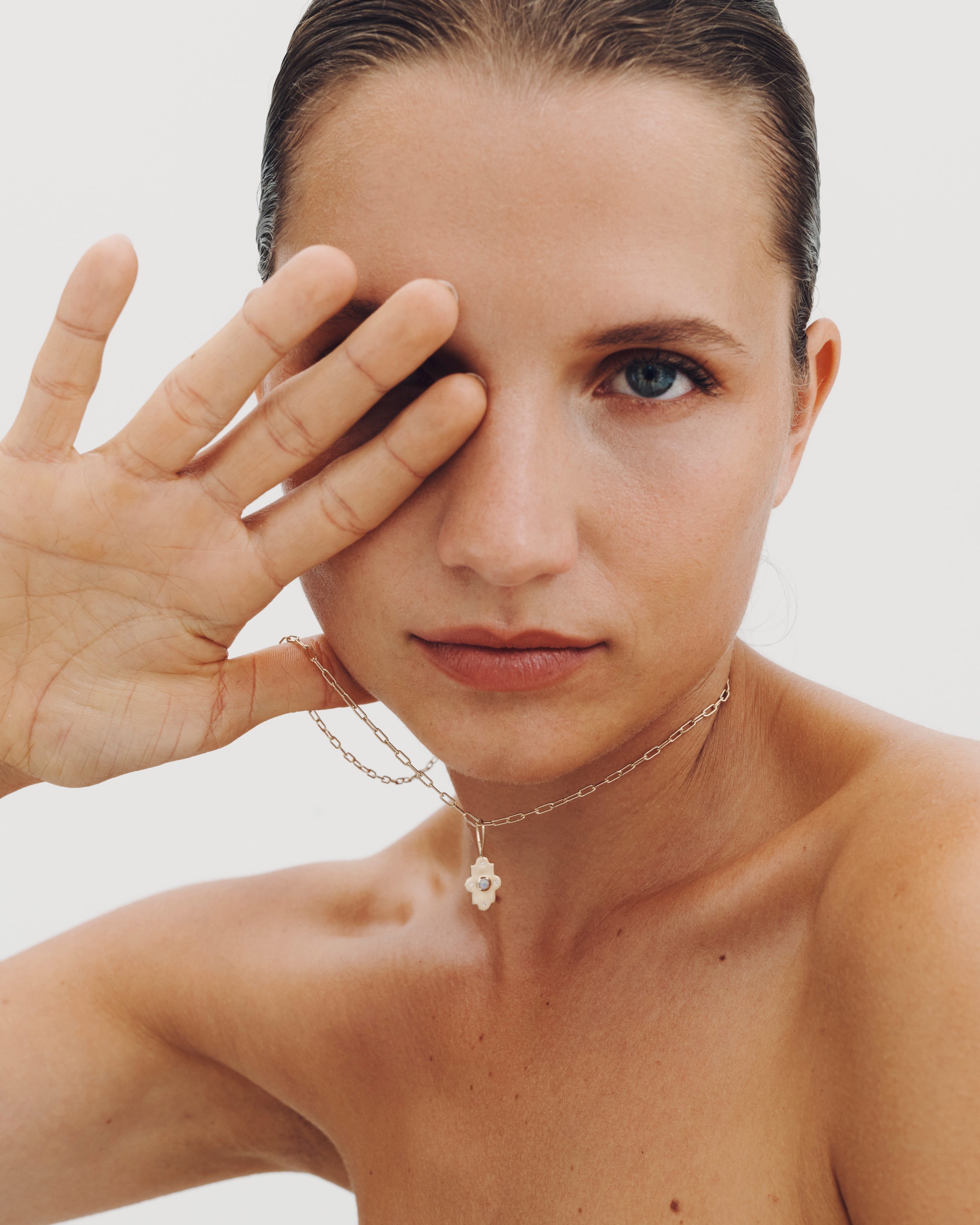Woman with a hand covering her eye against a plain background