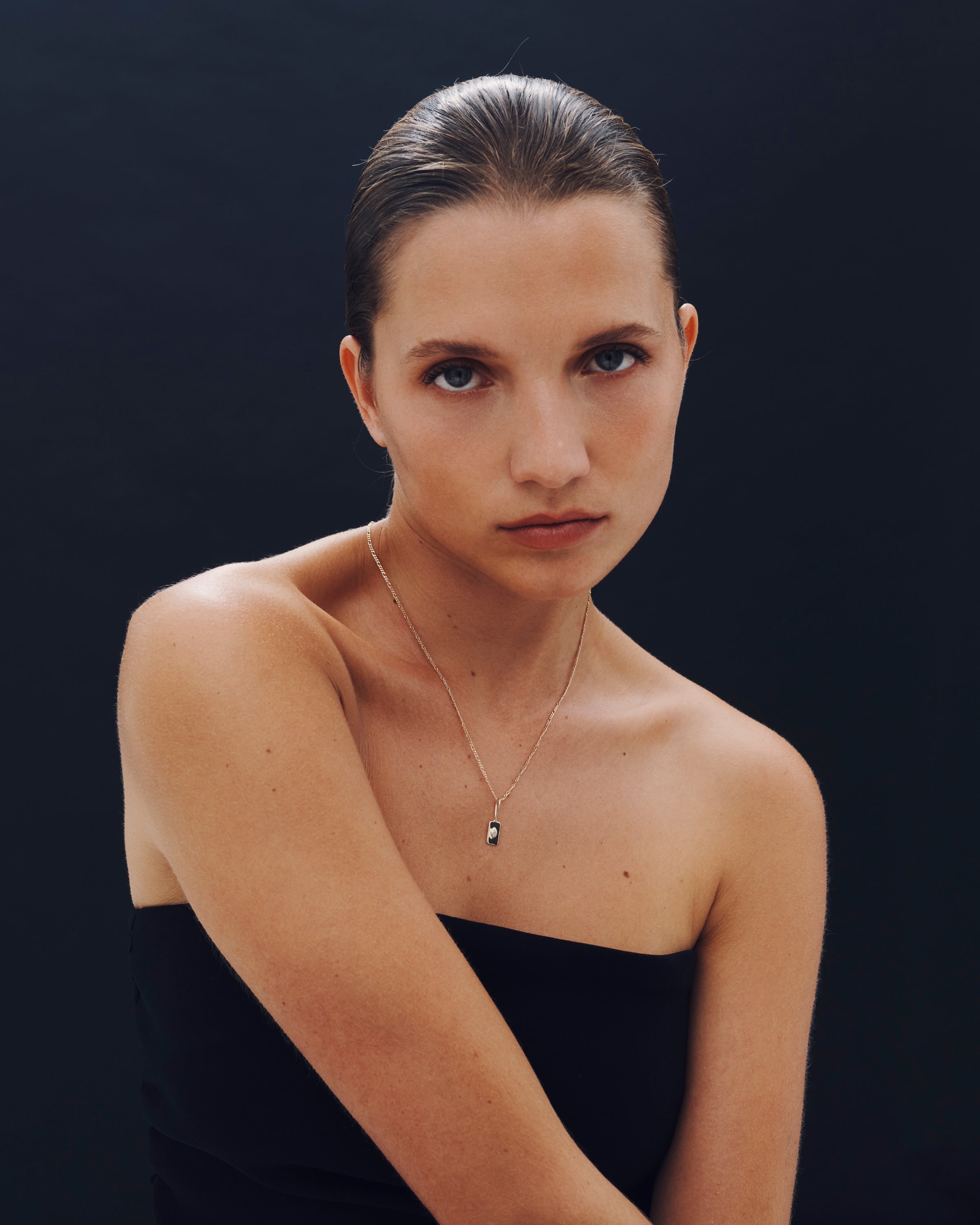 Woman wearing a black strapless top and gold necklace against a dark background