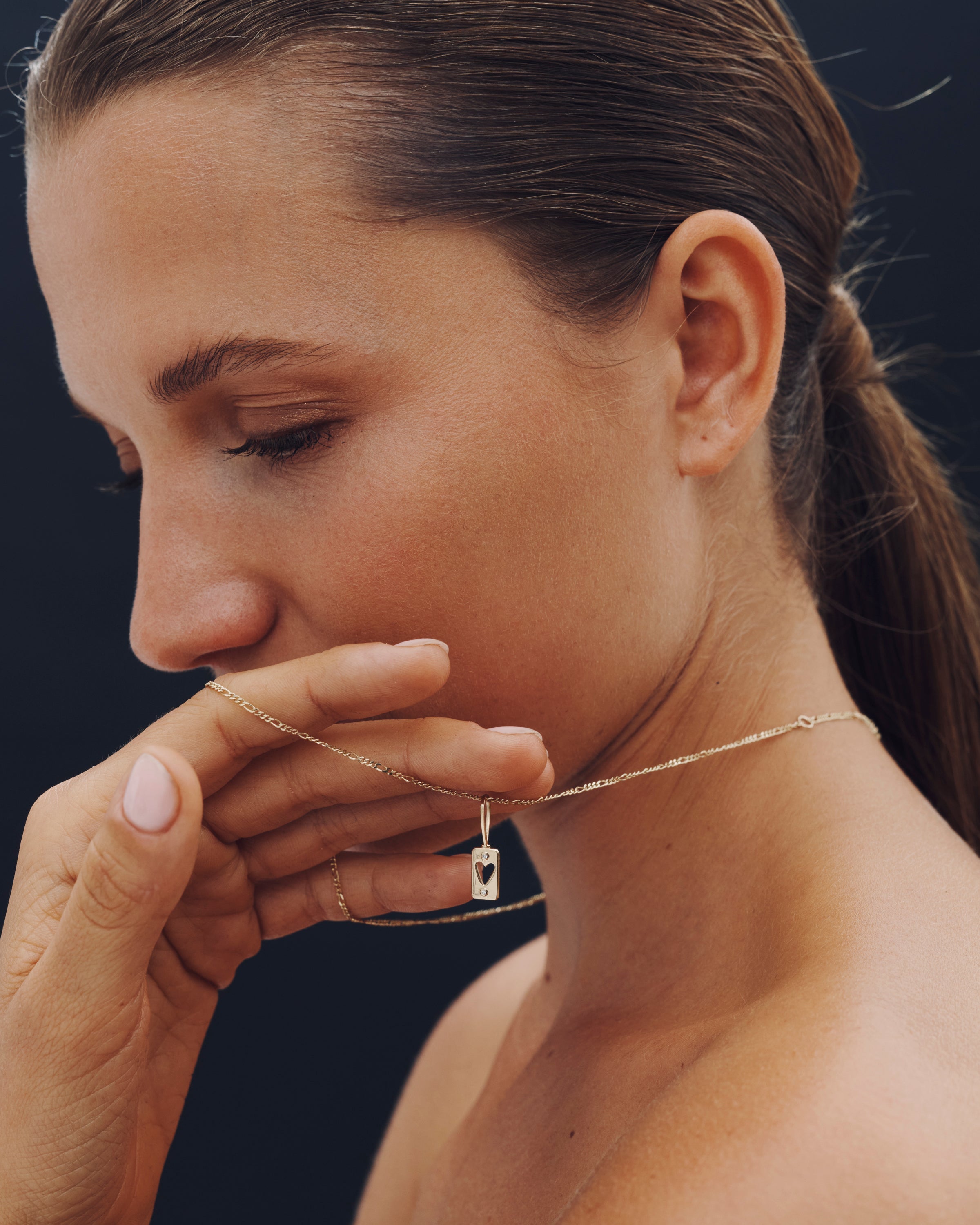 Woman wearing a necklace with a heart pendant against a dark background