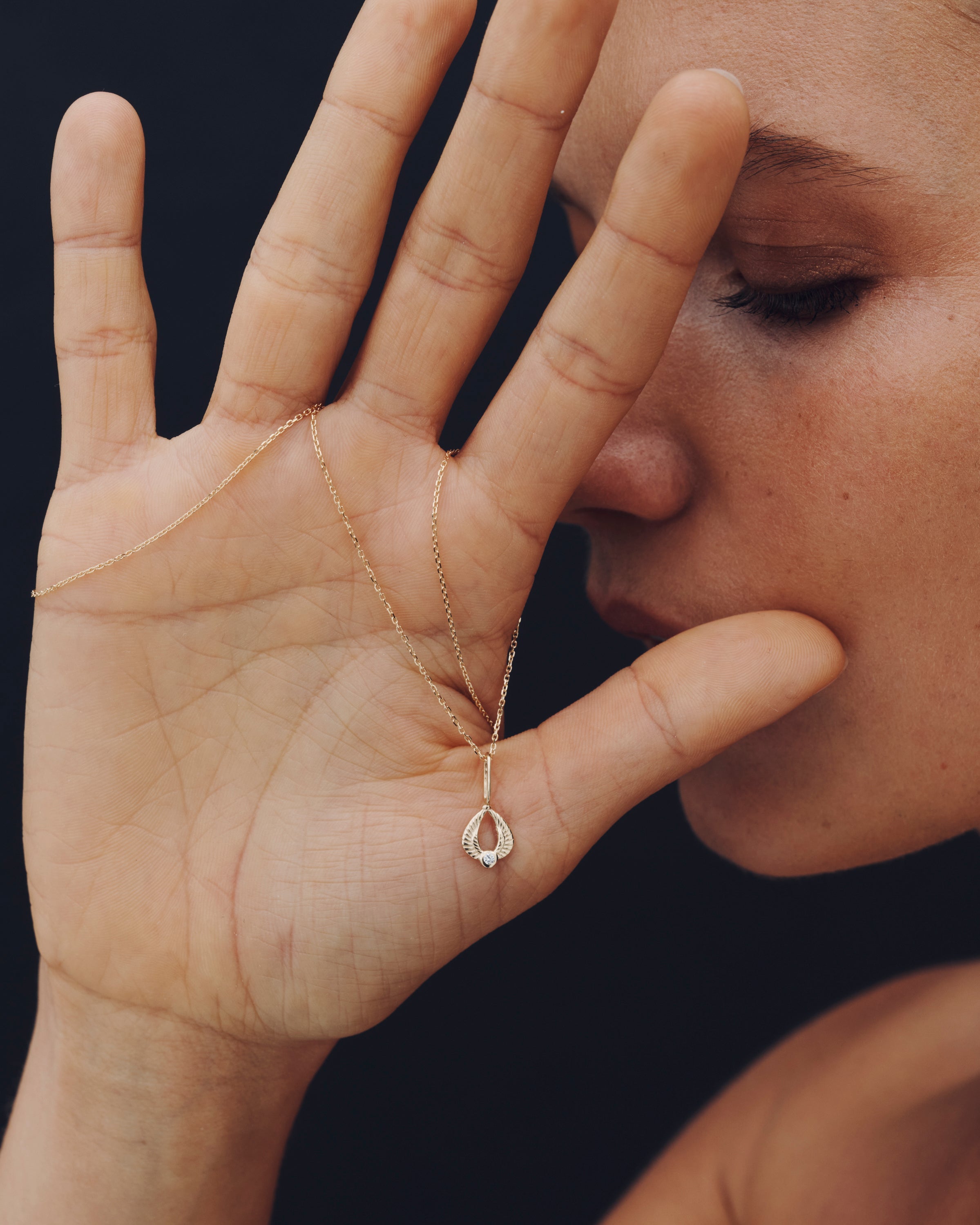 Person wearing a gold necklace with a teardrop pendant against a dark background