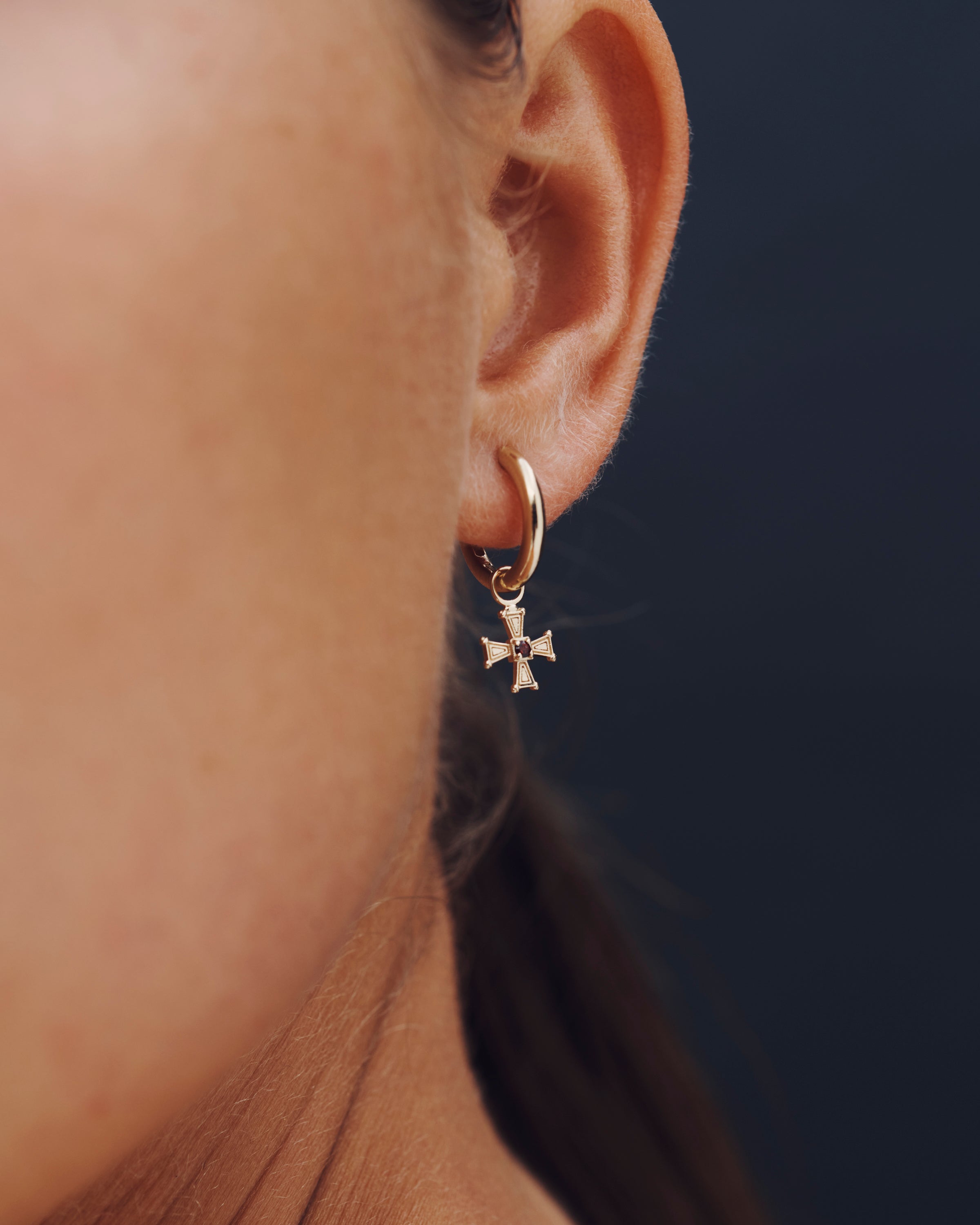 Close-up of an ear wearing a gold hoop earring with a star charm against a dark background