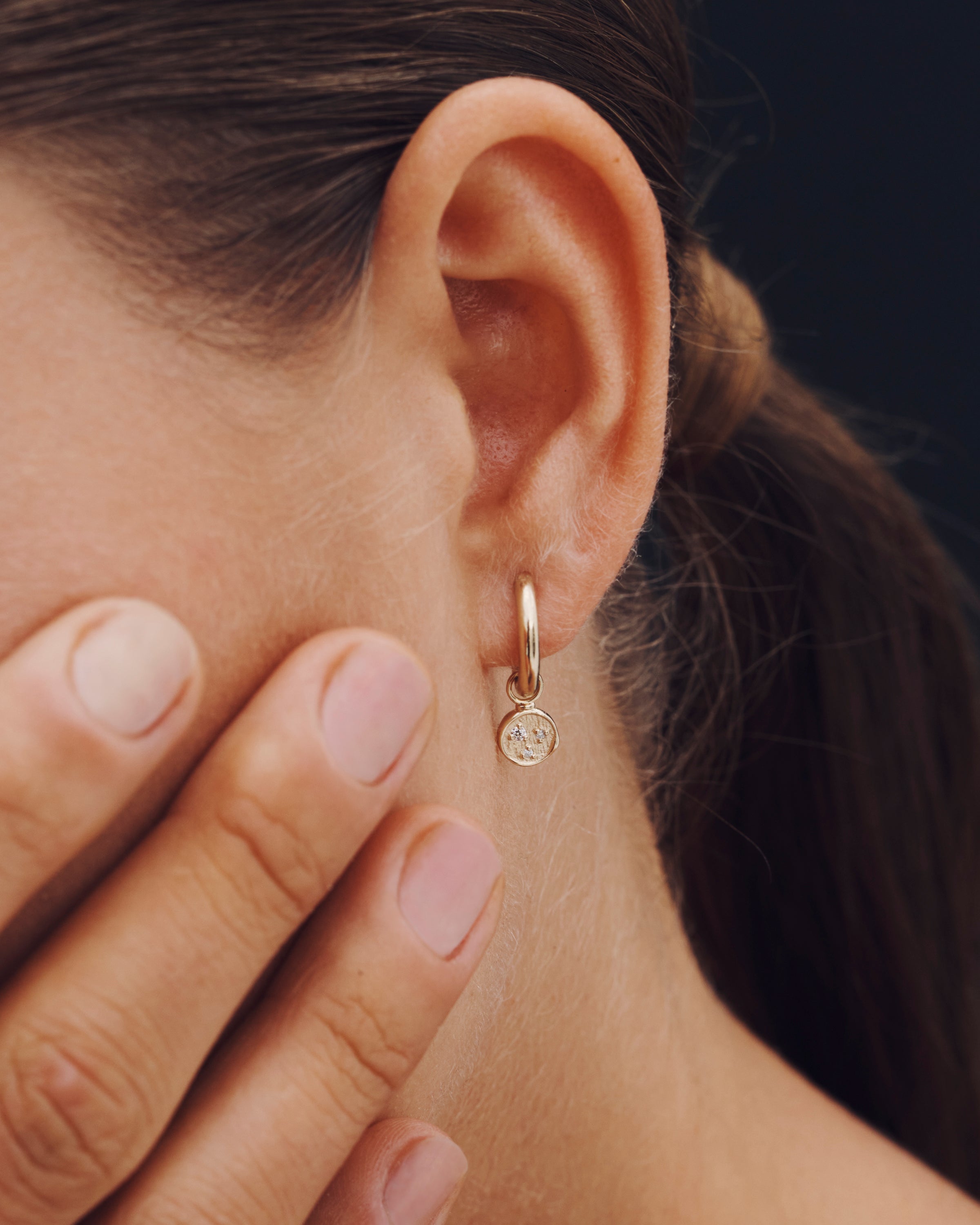 Close-up of an ear wearing a small hoop earring with a dark background