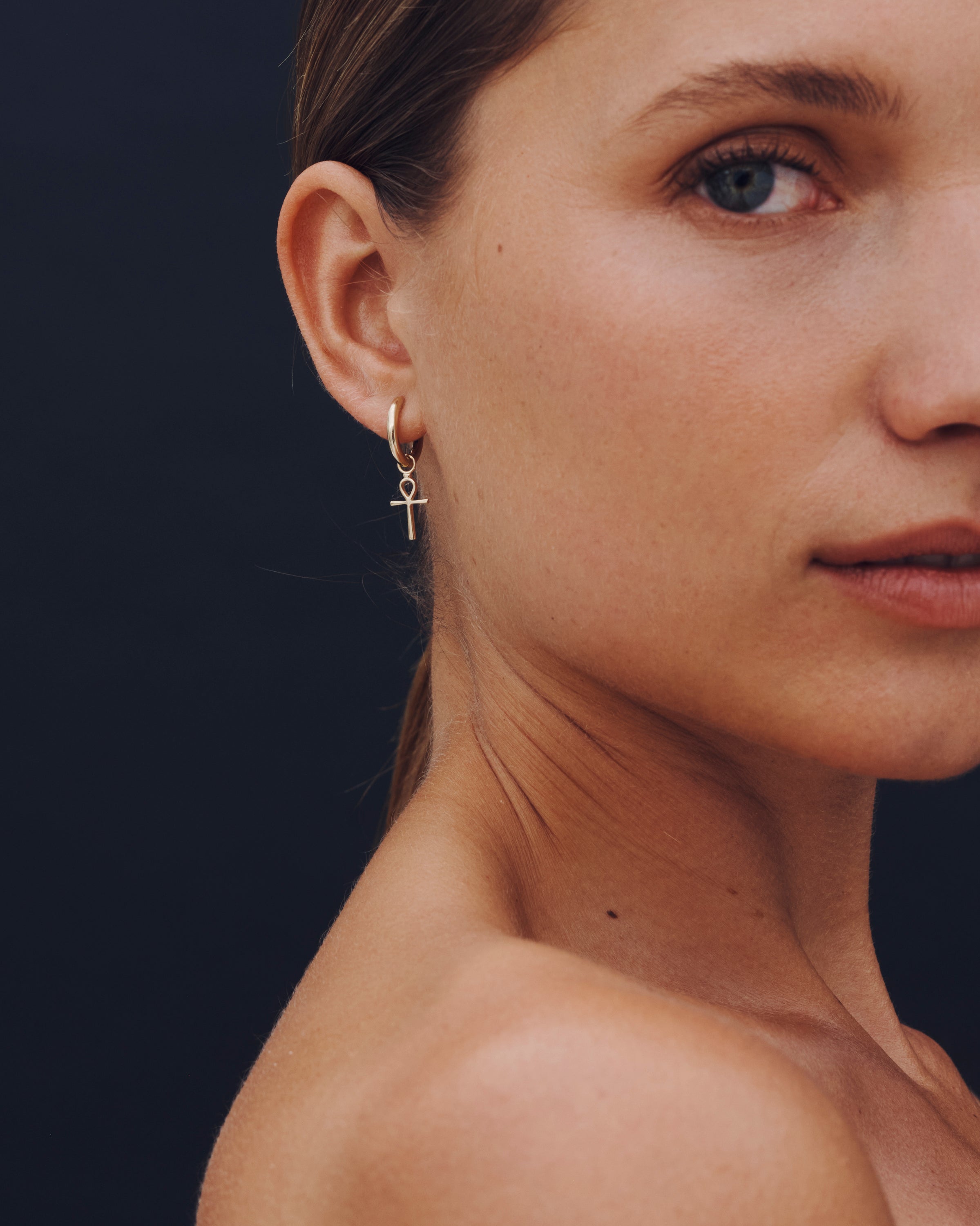 Close-up of a woman wearing a gold cross earring against a dark background