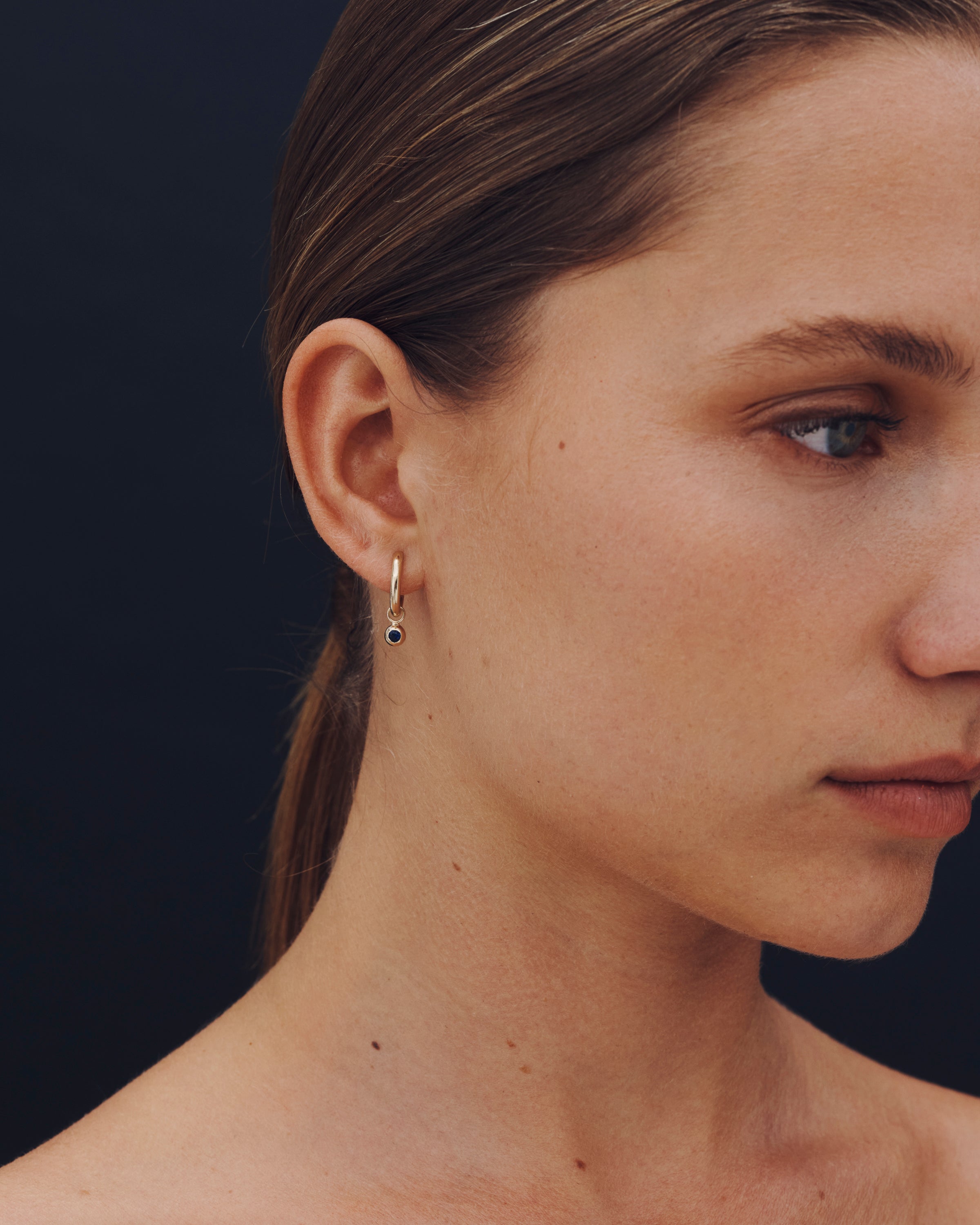 Close-up of a woman wearing a delicate earring against a dark background