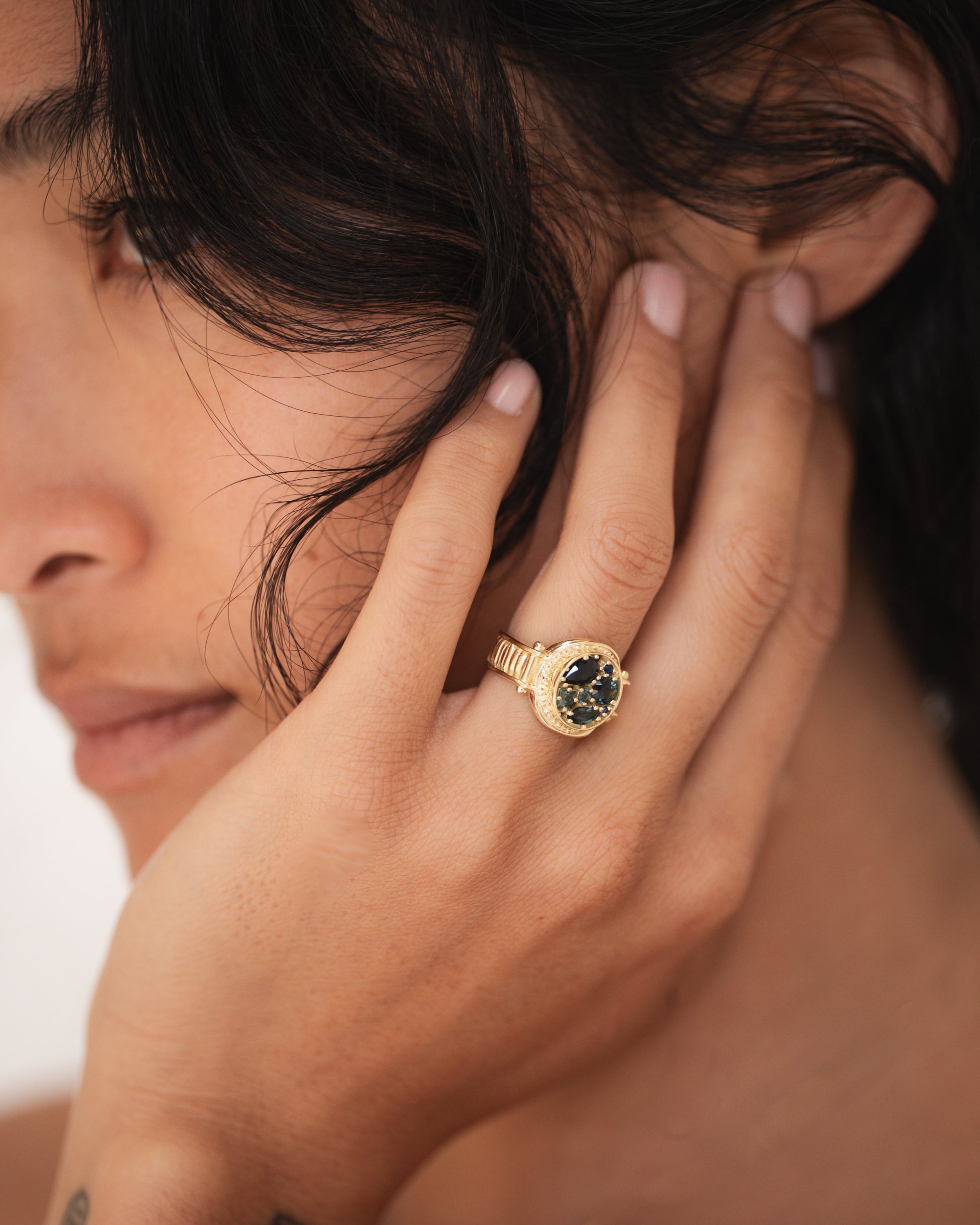 Close-up of a person wearing a gold ring with a gemstone, touching their hair.
